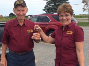 A man and woman in maroon shirts standing next to a car.