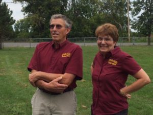 Two people in maroon shirts standing in a field.