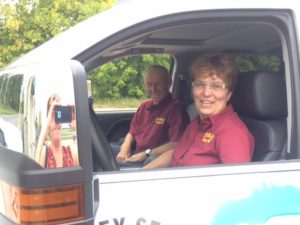 Two people sitting in the driver's seat of a van.