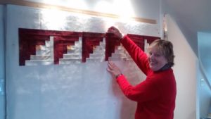 A woman is putting up a quilt on a wall.