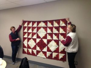 Two women standing next to a red and white quilt.