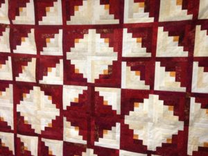 A red and white log cabin quilt hanging on a wall.