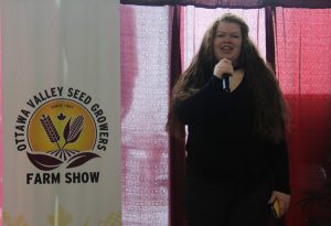 A woman is standing in front of a sign that says ottawa valley seed business farm show.