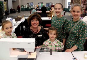 A group of people posing in front of a sewing machine.