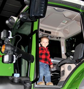 A small boy standing in the door of a green tractor.