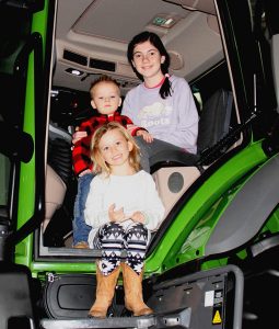 Three children sitting in the door of a green tractor.