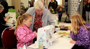 A group of girls and an older woman working on a sewing machine.