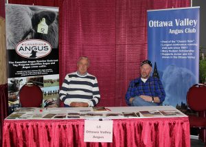 Two men sitting at a table in front of a banner.