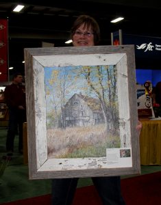 A woman holding up a framed painting.