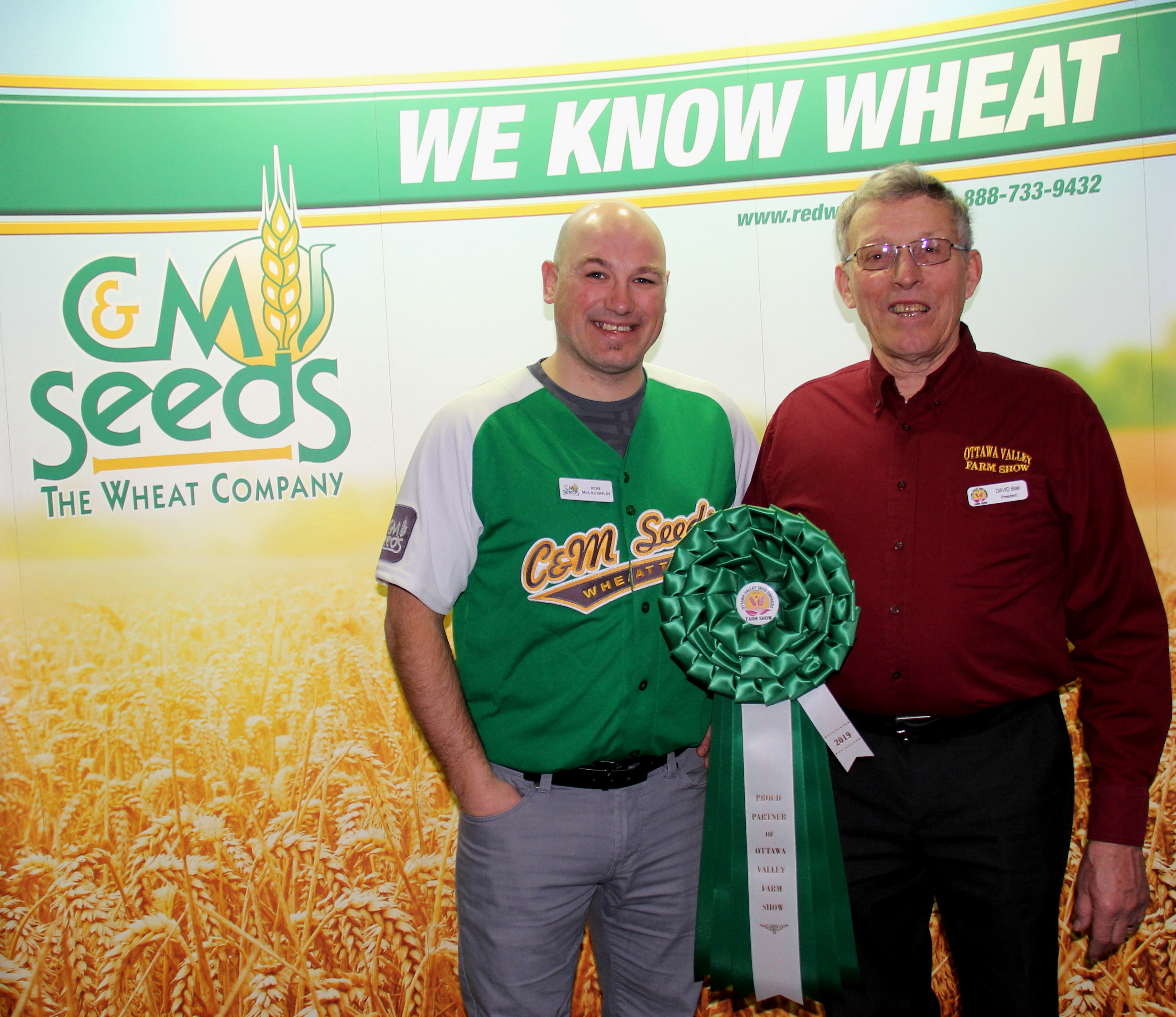 Two men standing in front of a sign with wheat on it.