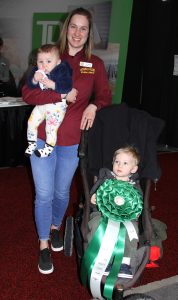 A woman holding a baby and a child in a stroller.