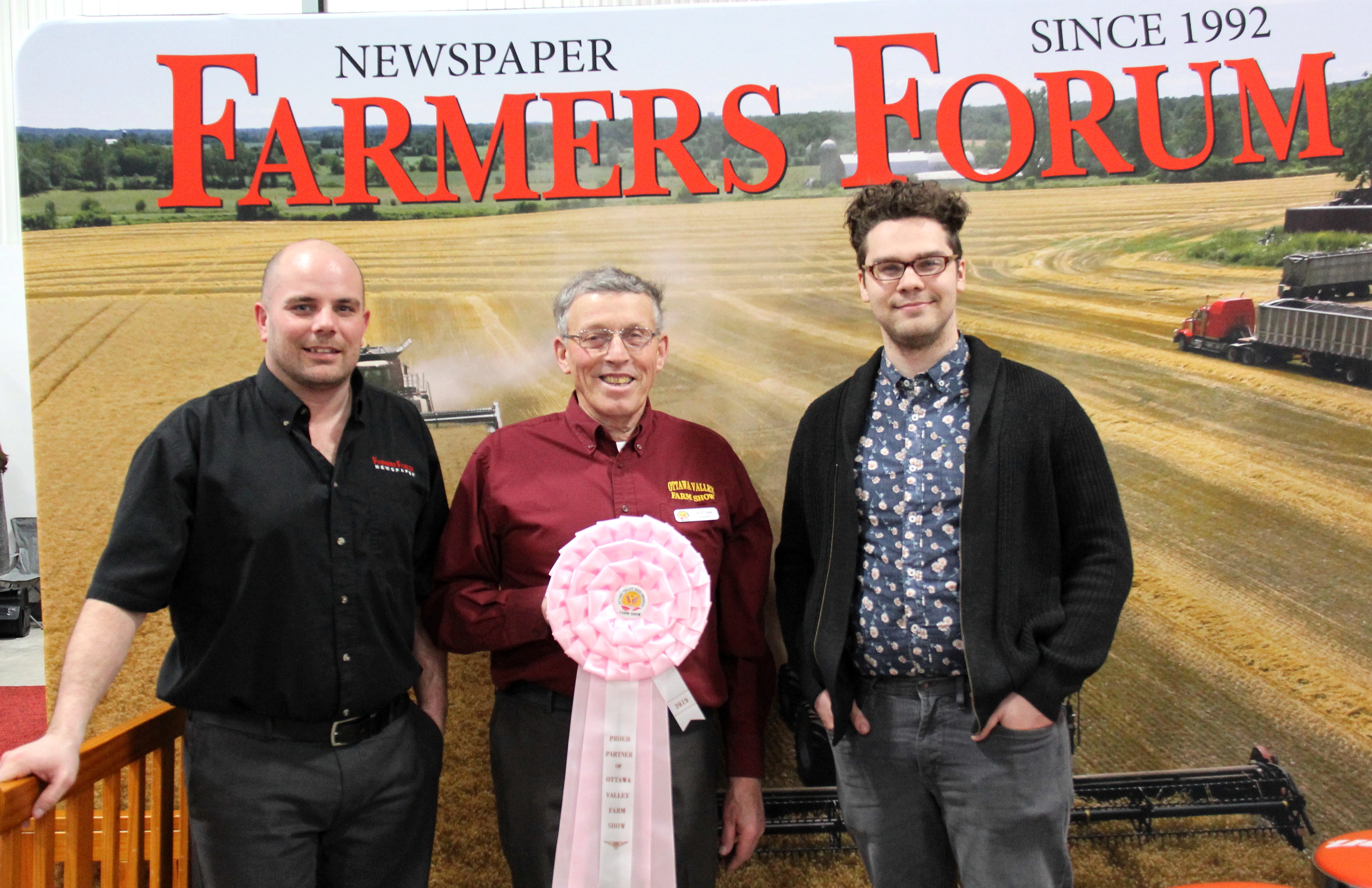 Three men standing in front of a farmers forum sign.