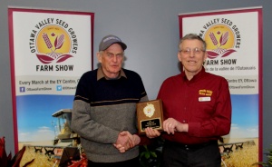 Two men holding a plaque in front of a wall.