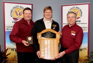 Three men holding a plaque and two are standing.