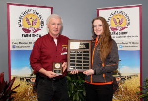 A man and woman holding a plaque in front of hay bales.