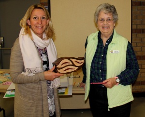 Two women holding a wooden object in front of each other.