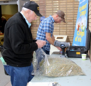 Two men standing at a table with hay.