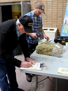 A man writing on paper next to another man.