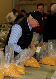 A man in black jacket holding onto bags of corn.