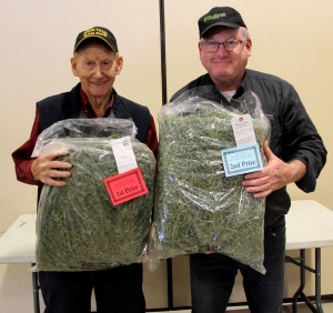 Two men holding bags of marijuana in front of a table.