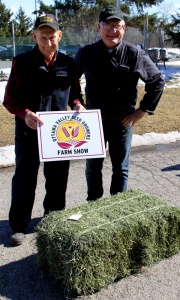 Two people standing next to a pile of hay.