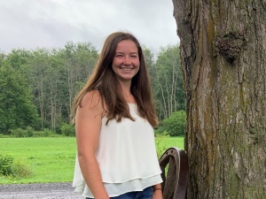 A woman standing next to a tree in front of a field.